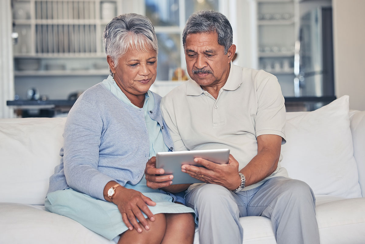 A man and woman looking at a hand held device on a couch in their home
