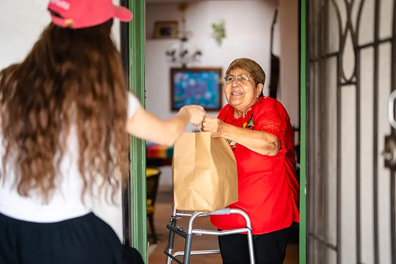 Young woman delivering meal in a paper bag to a woman at her house.