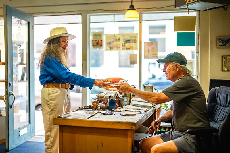 Shop worker handing a book to a woman in a shop.