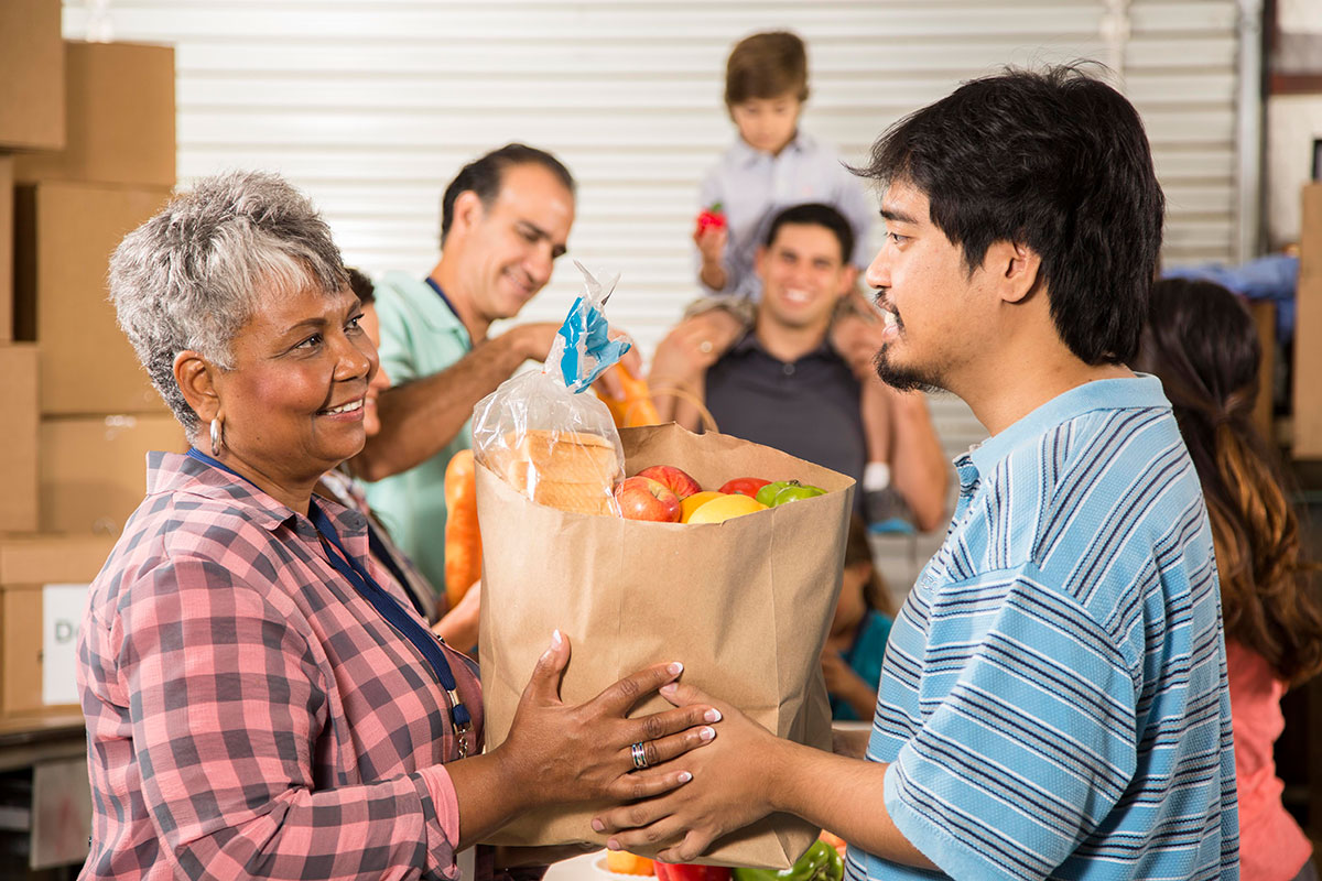 volunteer-with-food-bag Volunteer with grocery bag handing it to a hispanic woman