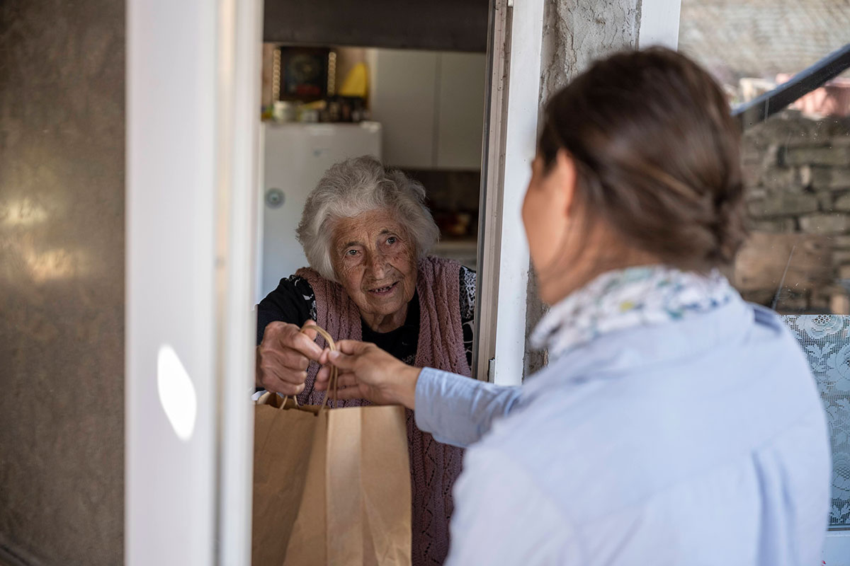volunteer delivers a grocery bag to an elderly woman at her doorstep