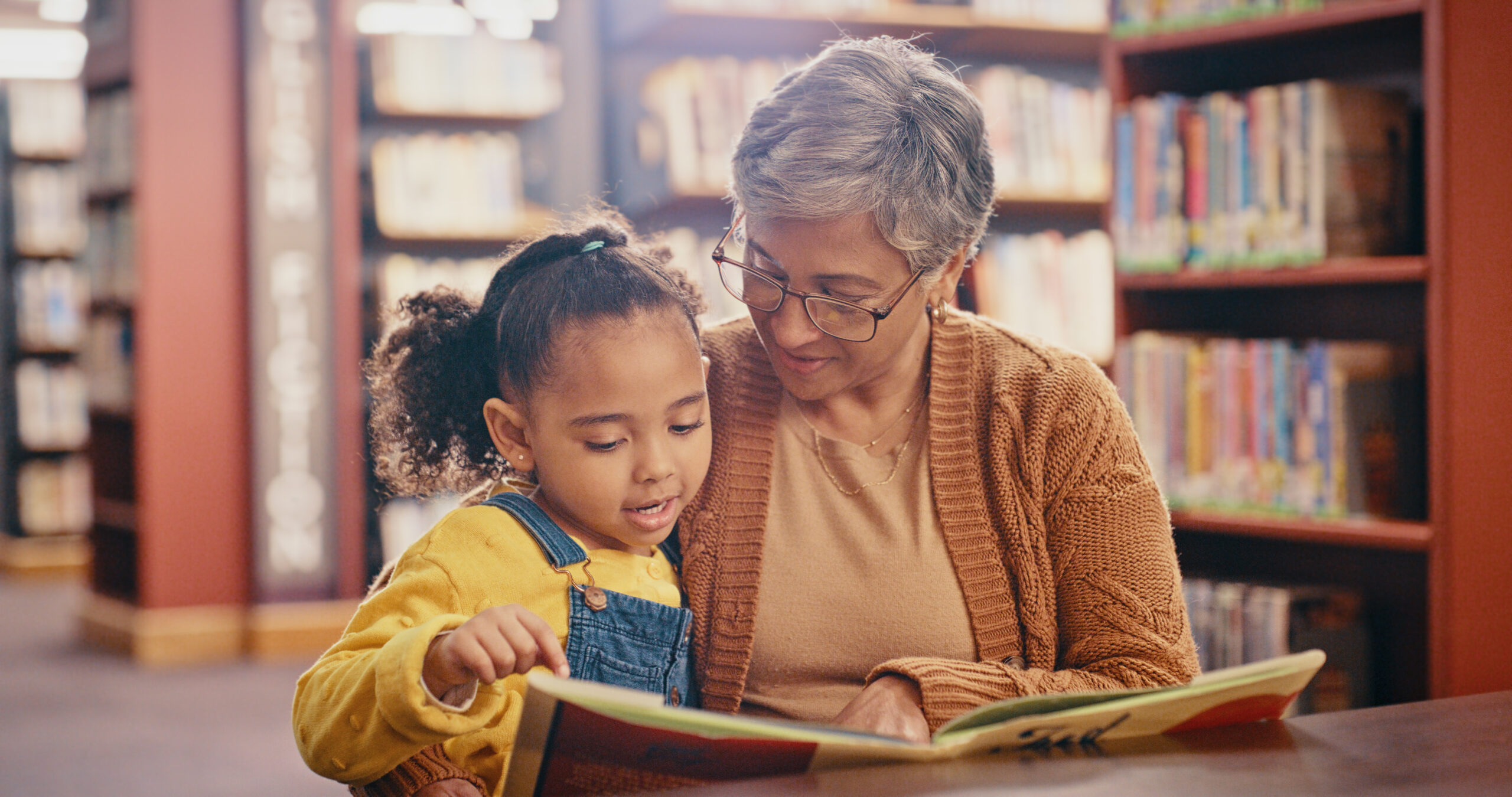 Library, book and grandma with grandchild, learning and reading while having fun together. 