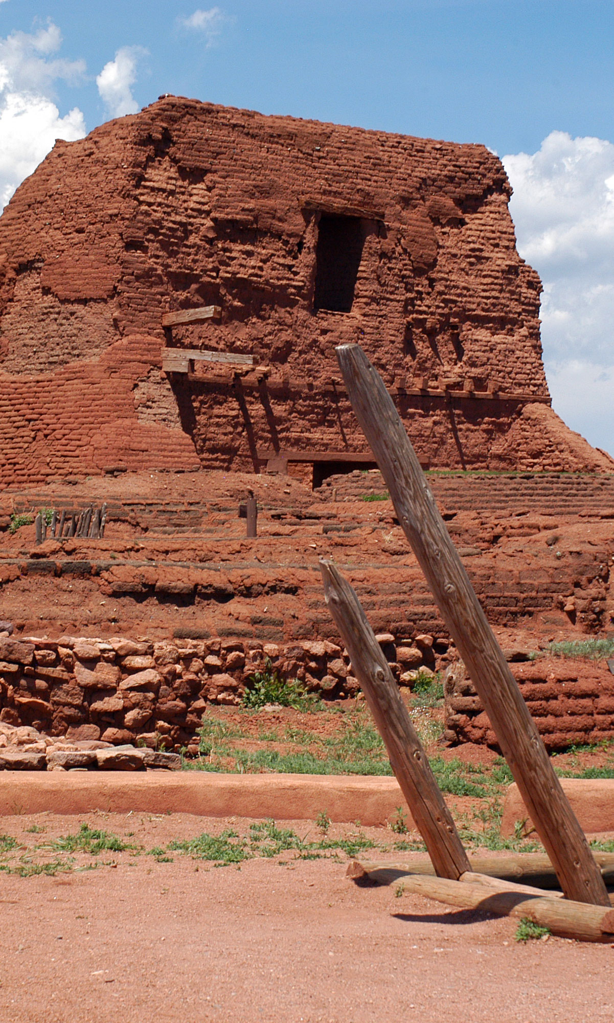 Pecos National Monument. A large red brick adobe structure with a native amerivan kiva in the forground. There is a ladder coming through the roof of the Kiva. This is an ancient structure.