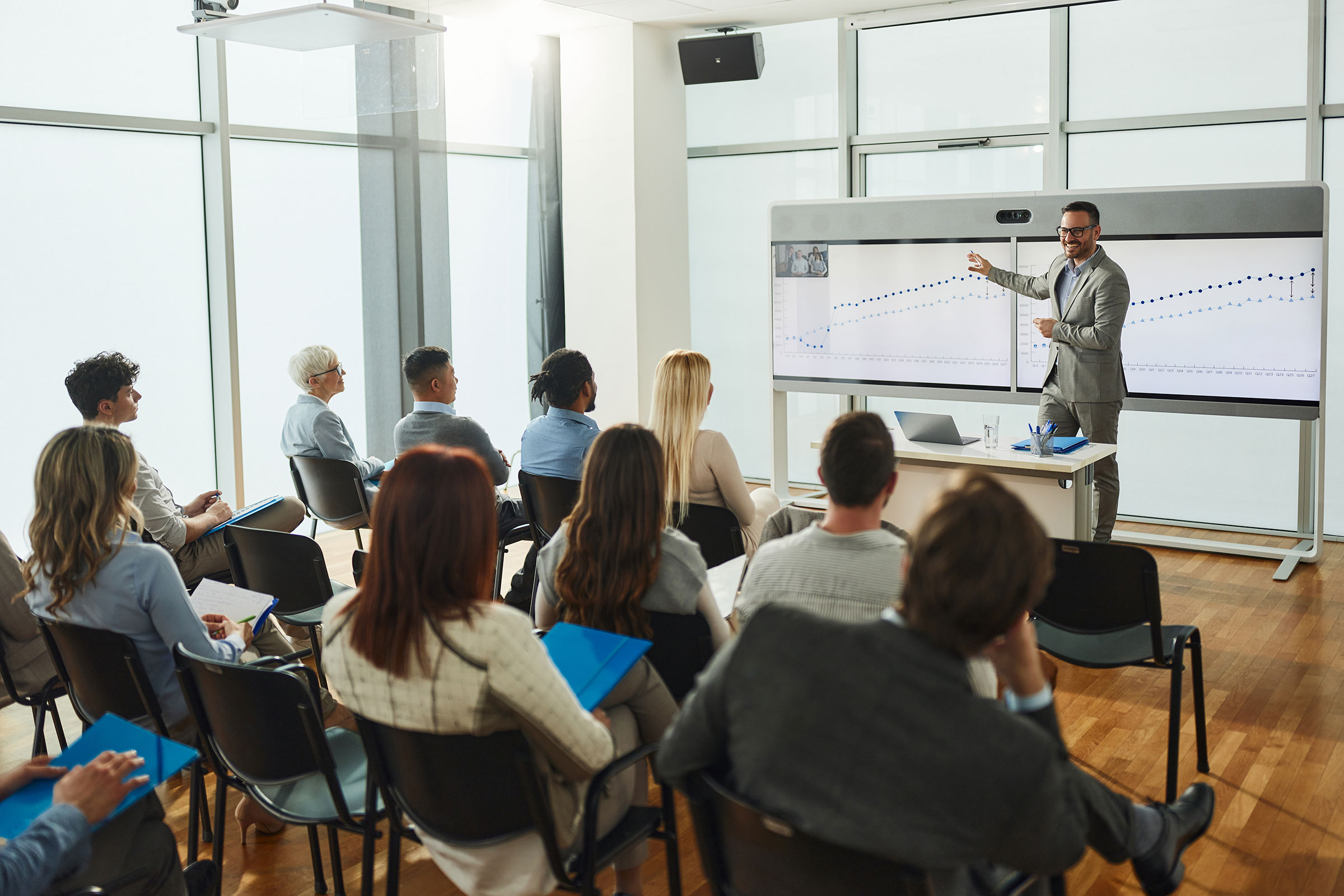 a man teaching at a large board in front of a diverse audience or class.