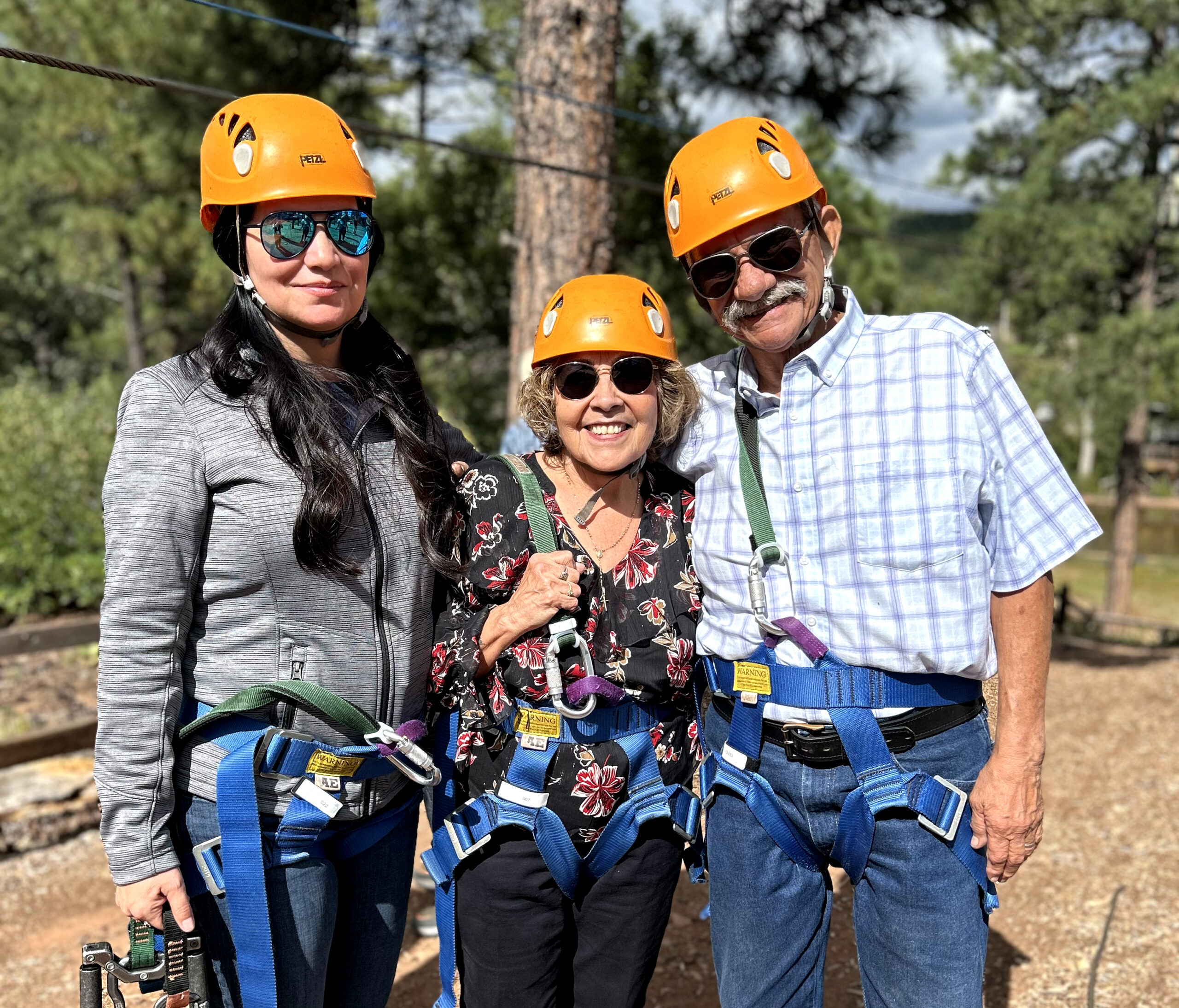 Two women and one man wearing orange helmets prepare to go ziplining.