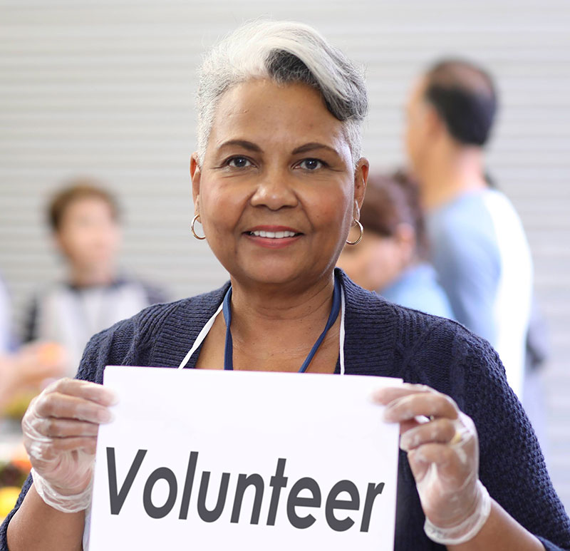 A woman with greay hair holding a sign that says voluteer